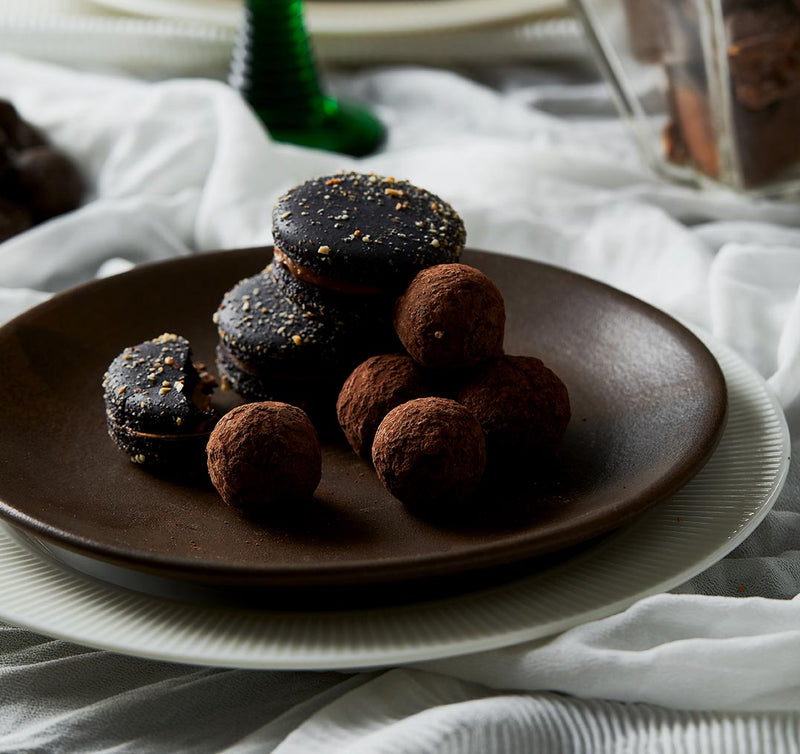 A table setting with a close of a plate stacked with milk chocolate and honeycomb macarons and chocolate truffles