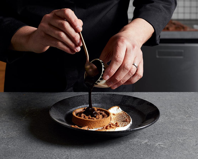 A pastry chef pouring dark chocolate ganache into a tart shell