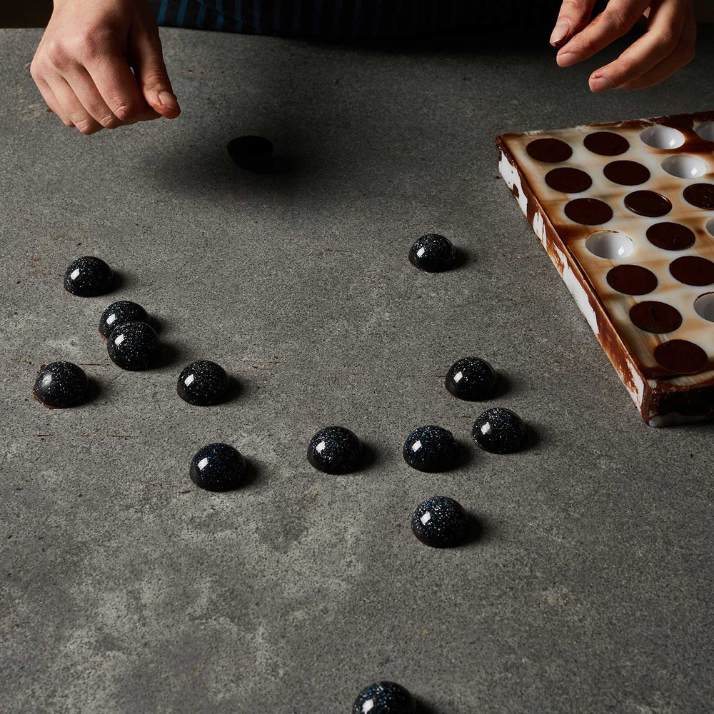 A chocolatiere demoulding a tray of shiny dome shaped chocolate bonbons