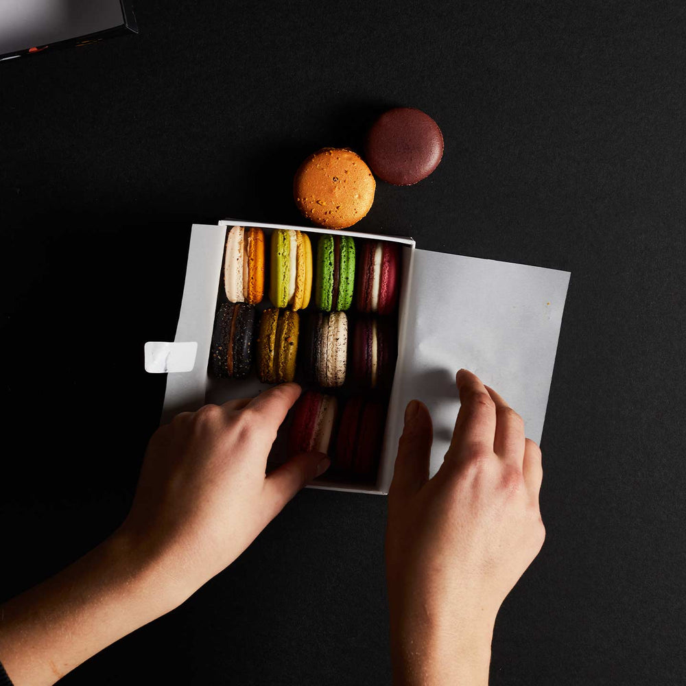 An images showing a person packing a macaron box with a selection of colourful macarons