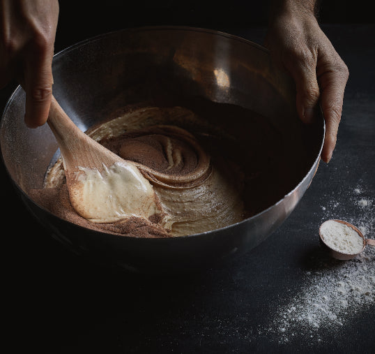 A pastry chef mixing a buttercream filling with a wooden spatula