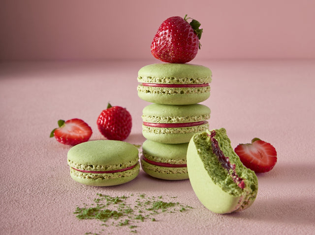 Strawberry and Matcha macarons with pale green matcha shells and strawberry filling, styled with fresh strawberries on a soft pink background.