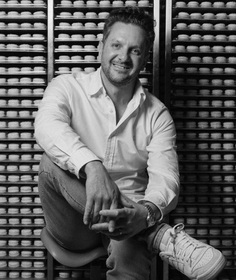 Black and white profile image of Tim Clark, Creative Director of CACAO in front of a wall of macarons